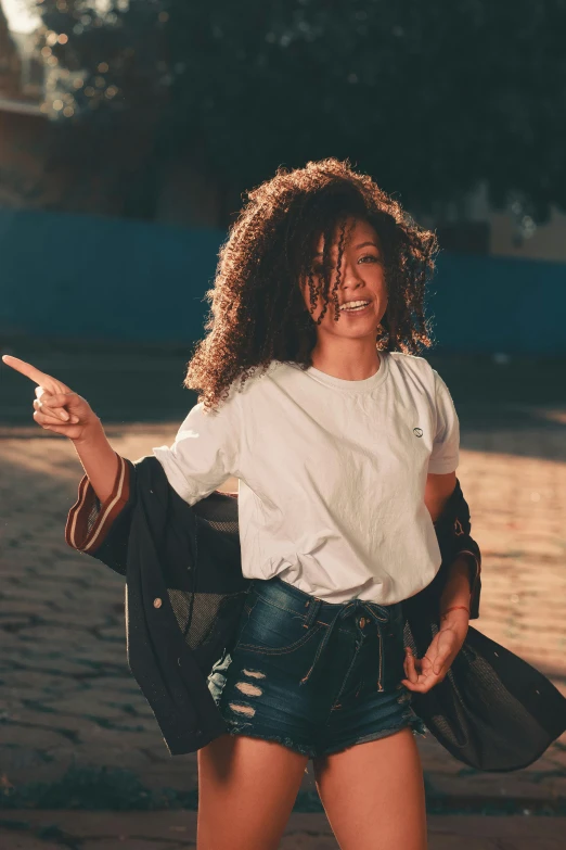 a woman in a white t - shirt, blue shorts and black jacket is pointing