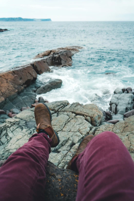 someone wearing hiking shoes standing on some rocks near the ocean