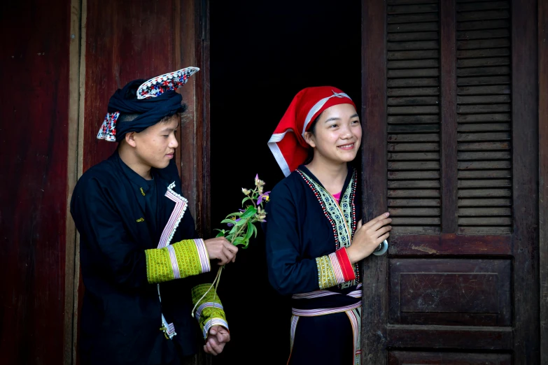 two people in traditional thai clothing with flowers near the door