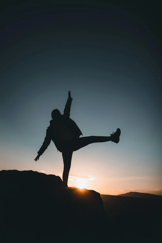 a person standing on top of a cliff with a leg in the air