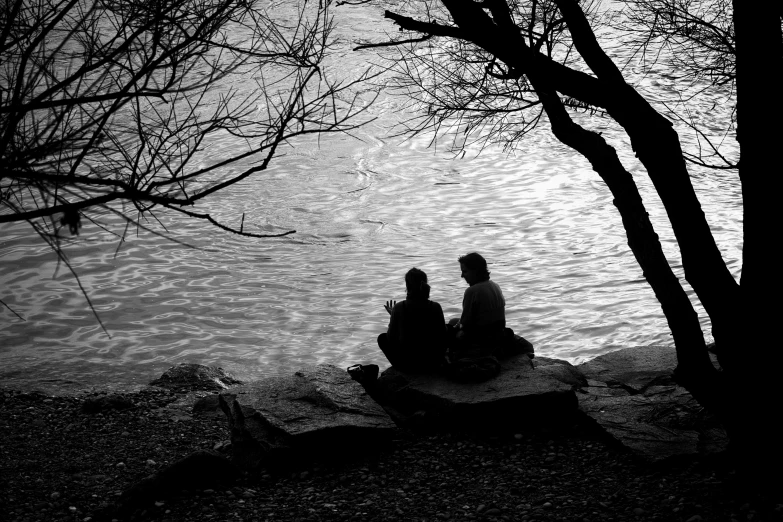 a black and white po shows two people sitting beside the water