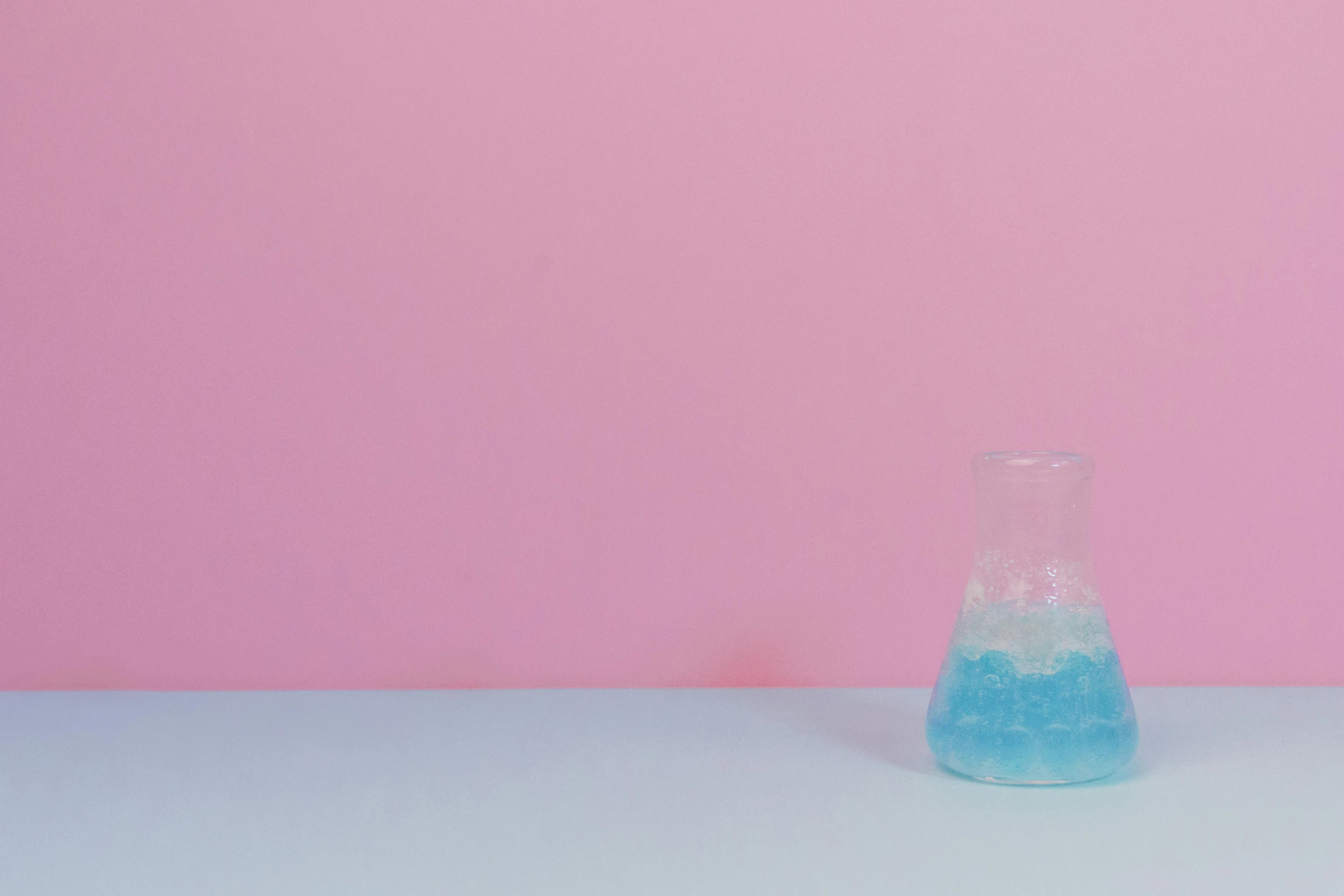 a blue liquid filled vase next to a pink wall