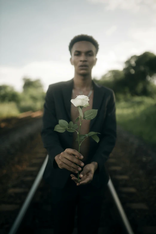 a man is holding a white rose while standing in the middle of a railroad track