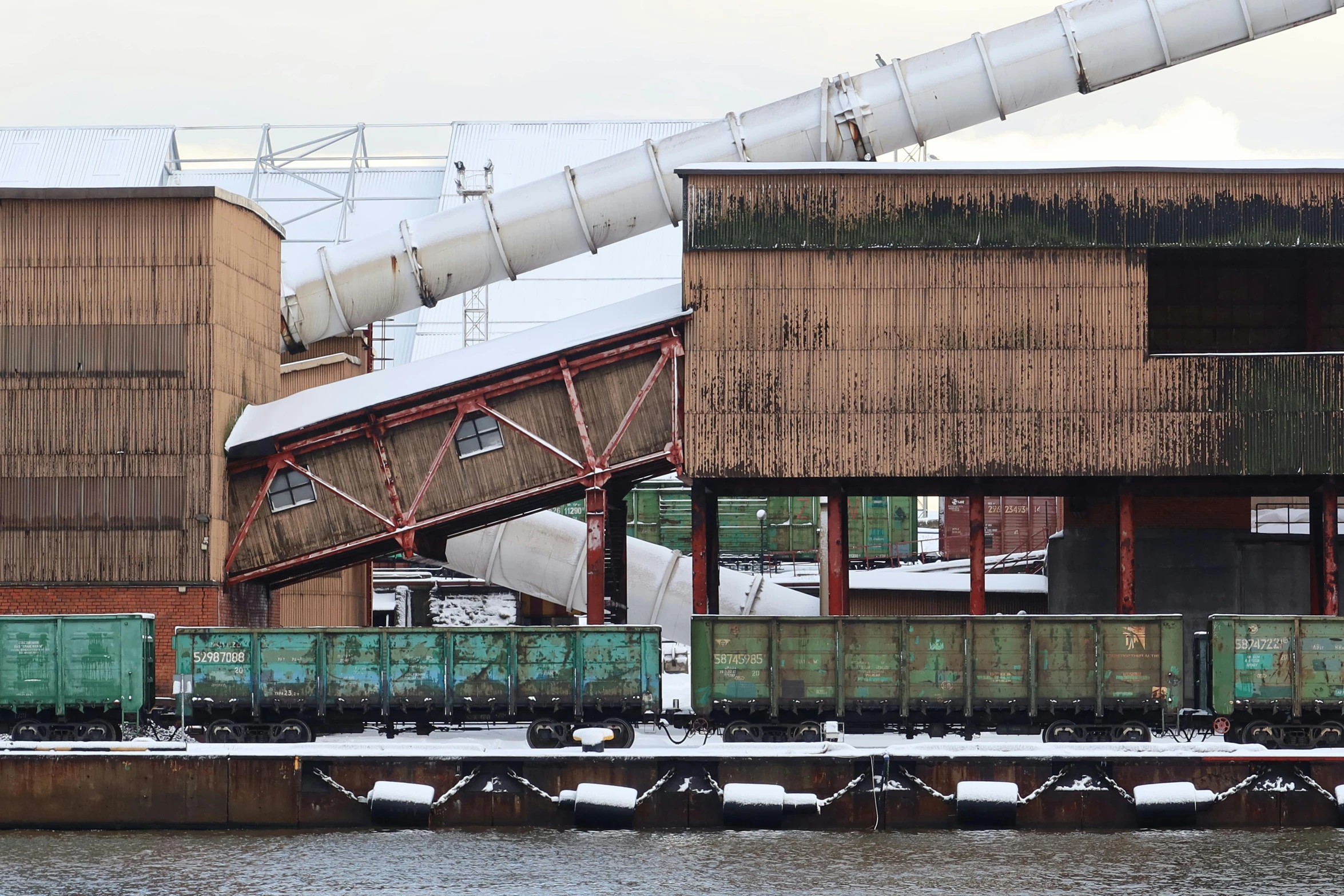 an industrial train sits outside a large building with metal pipes and green doors