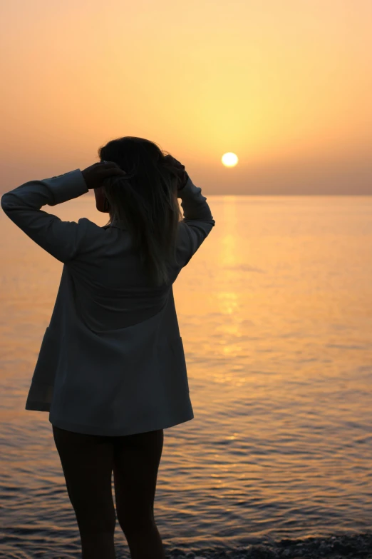 a beautiful woman stands by the water at sunset