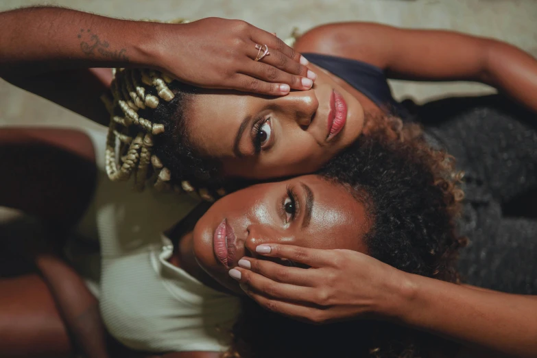 two girls laying down, one is touching her face with the other