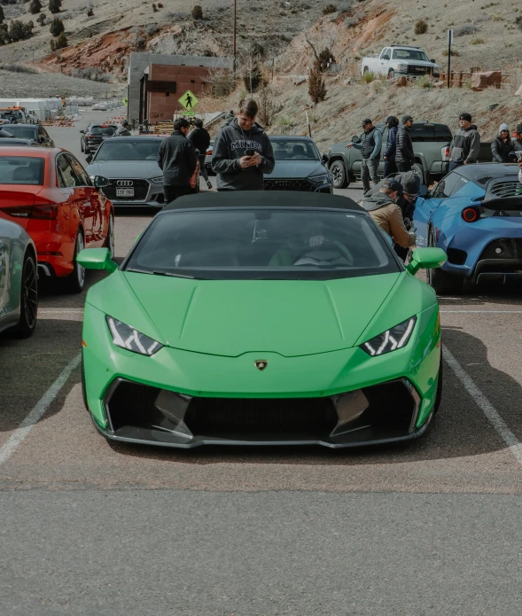 green sports car parked in parking lot with people standing around it