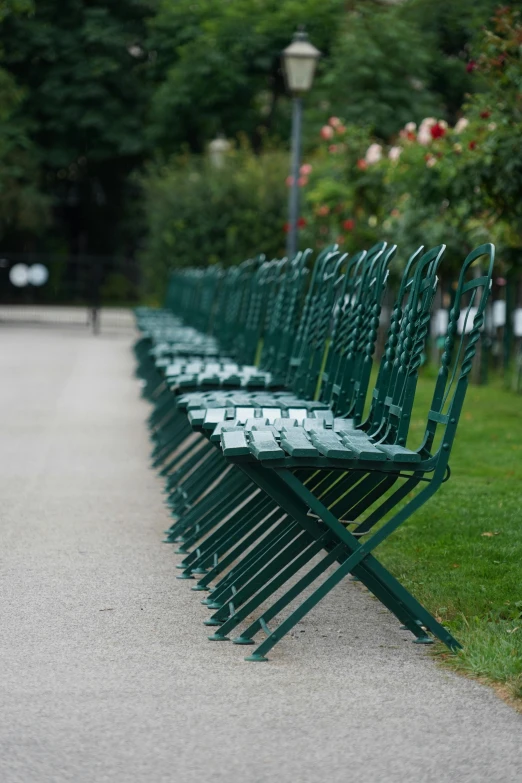 a row of green metal benches sitting next to each other on grass