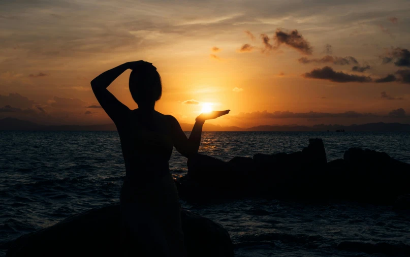 the woman poses in silhouette with her hand on her head