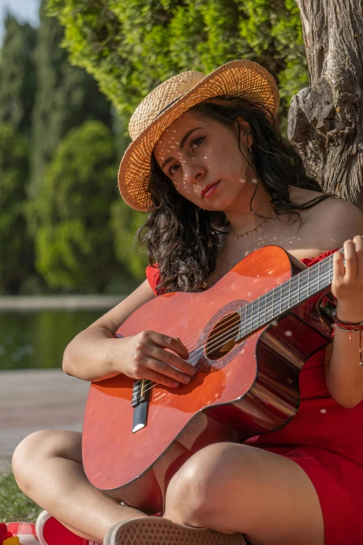 a woman with long hair sitting next to a tree with an orange guitar