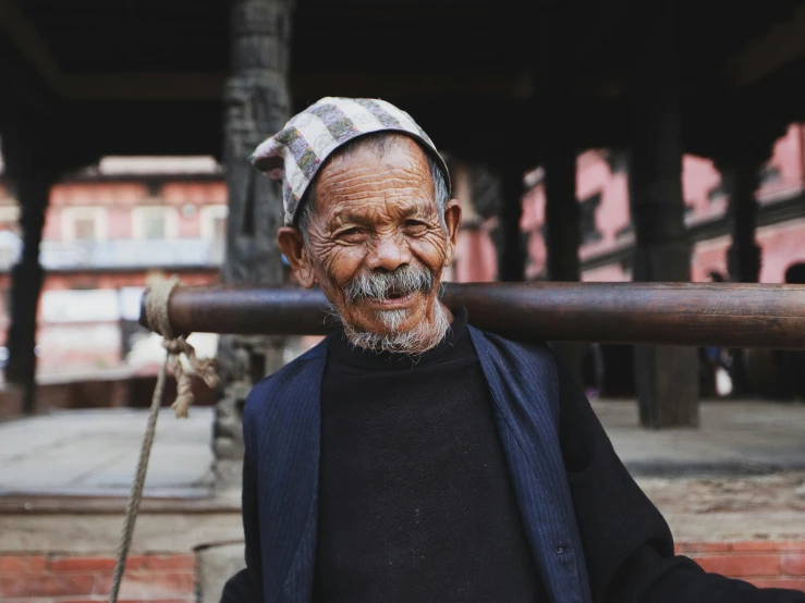 an old man wearing a hat, jacket and scarf holds a large long stick