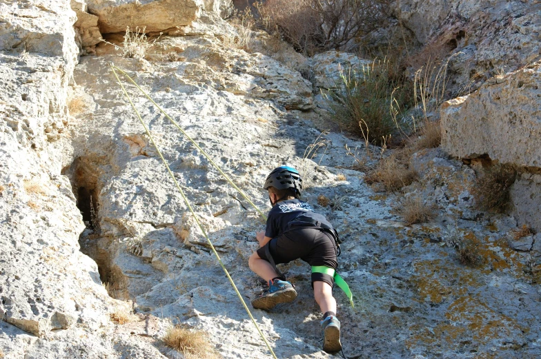 man climbing up rock while holding onto a rope