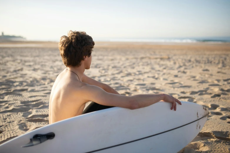 young man sitting on the beach with his surf board