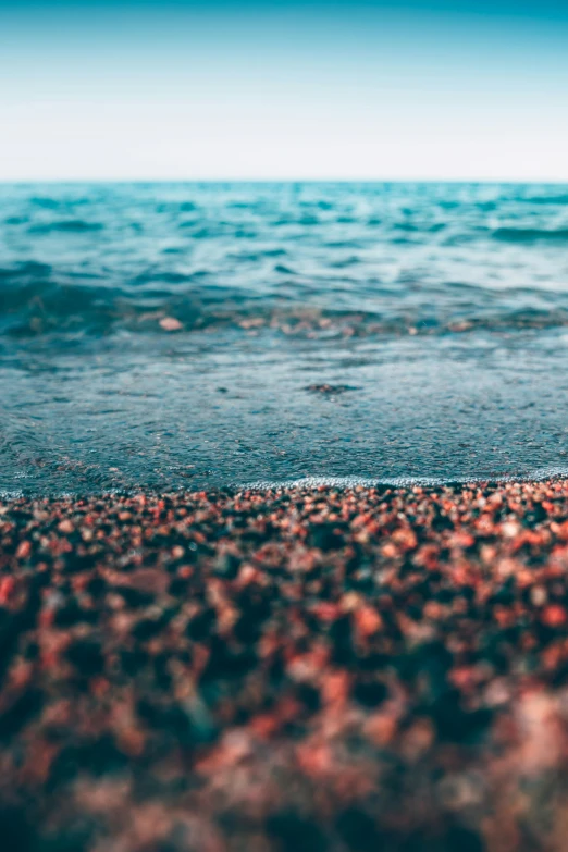 a picture of an ocean with small red rocks in the water