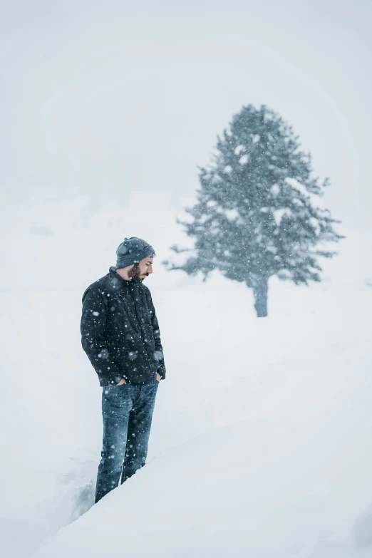 a man standing in the snow beside a small tree