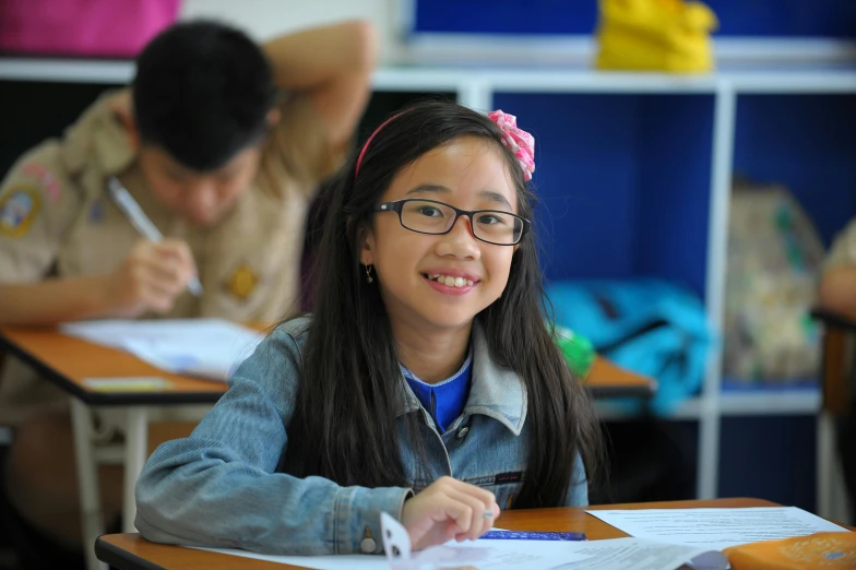 a little girl writing in a notebook while two others sit behind her