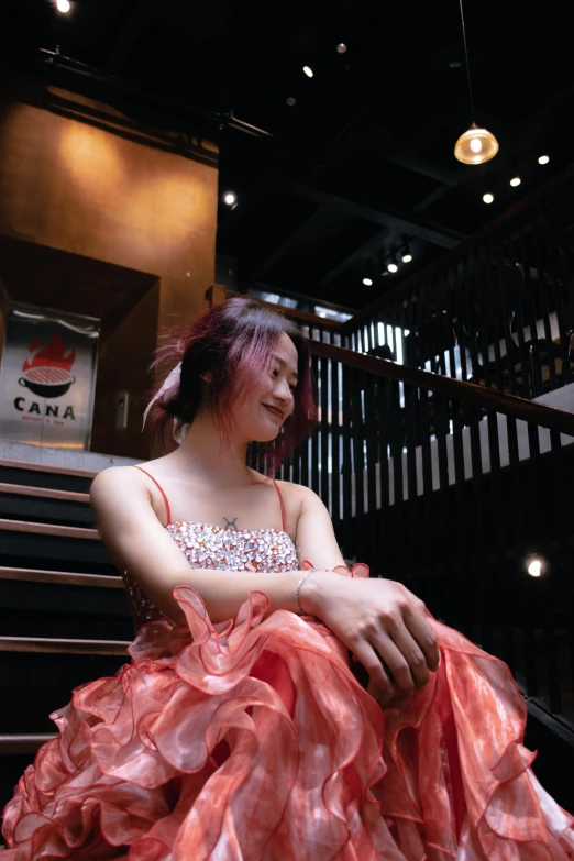 the girl sits on the stair case while wearing an orange dress