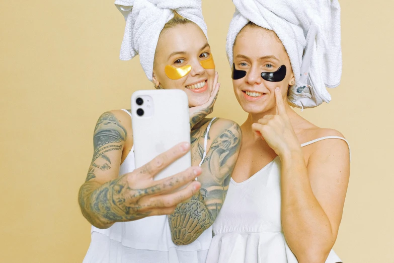 two women with tattoos are holding a cell phone and towel