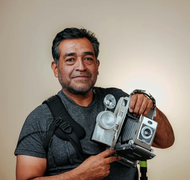 a man holding an old fashioned camera next to a wall