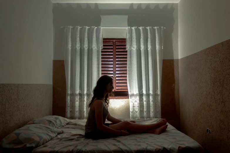 girl sitting on a bed looking out a window