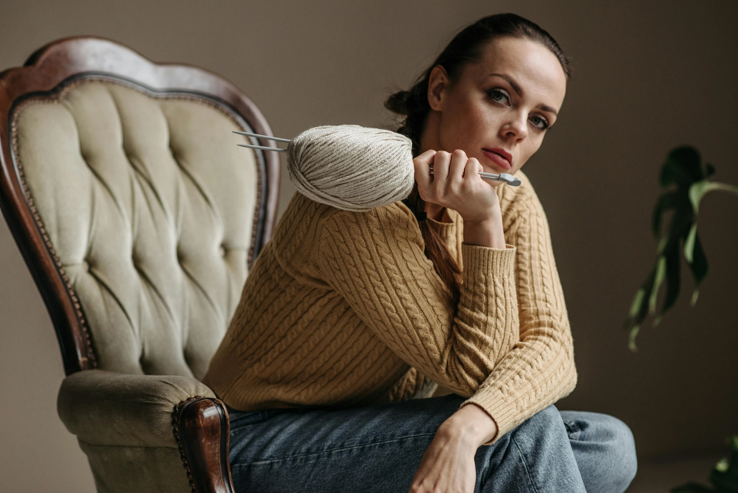 a woman sitting in a chair next to a plant holding soing up to her mouth