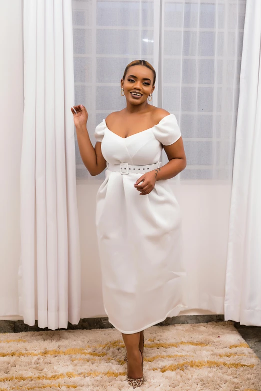 a woman wearing a white dress posing in front of a window