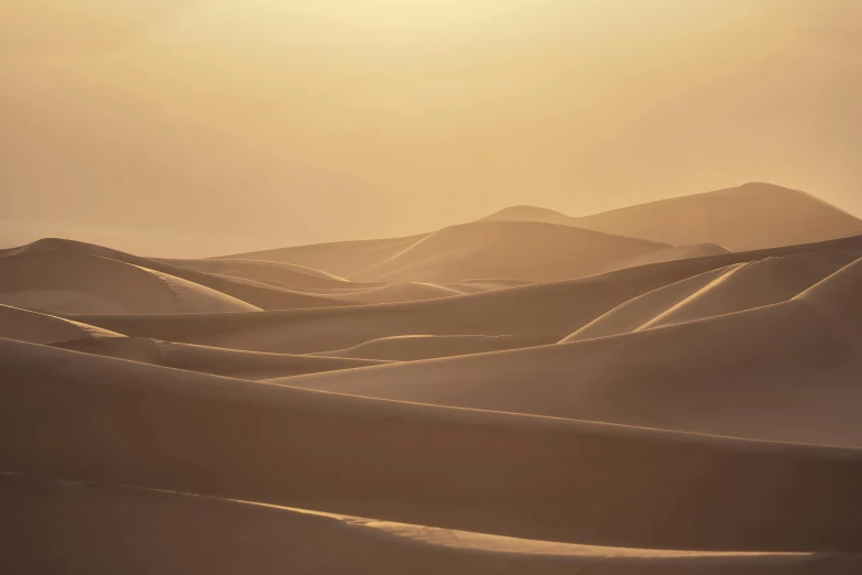 the sun rises over a landscape of sand dunes