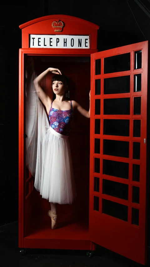 a girl in a tutu is posing inside a red phone booth