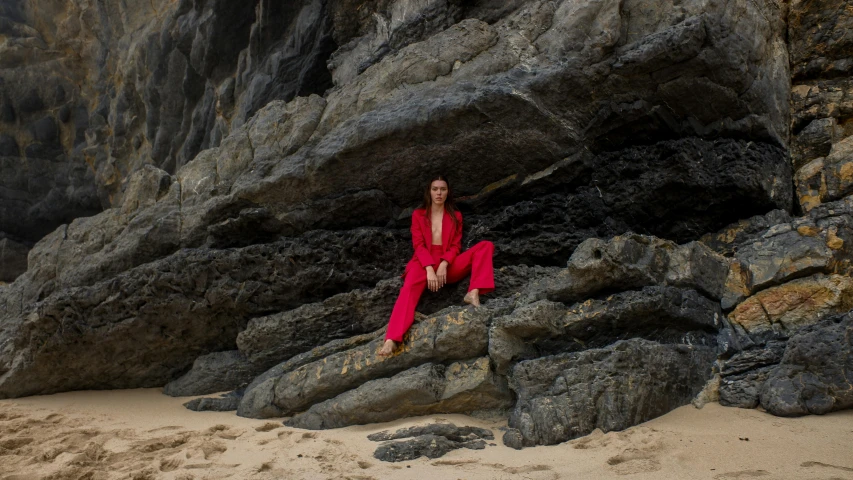 a woman sitting on rocks in a red suit