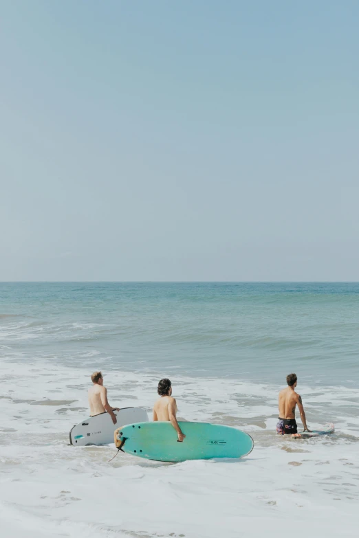 three young men with surfboards stand in shallow water on the beach