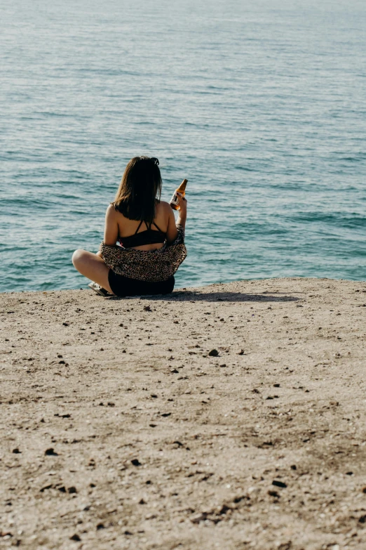 a woman in a bikini sits on the beach looking at her phone