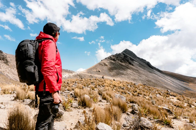 a man with a backpack standing on top of a dry grass covered hillside