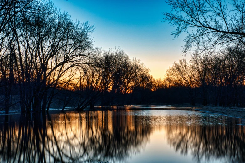 the sun is going down behind a small pond with some trees