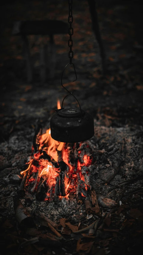 a pot is hooked to a chain over a campfire