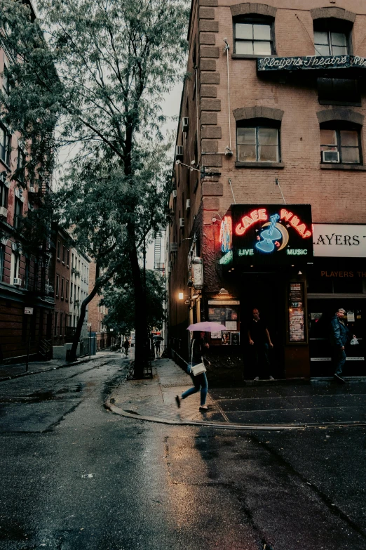 a wet street corner with people walking and a store