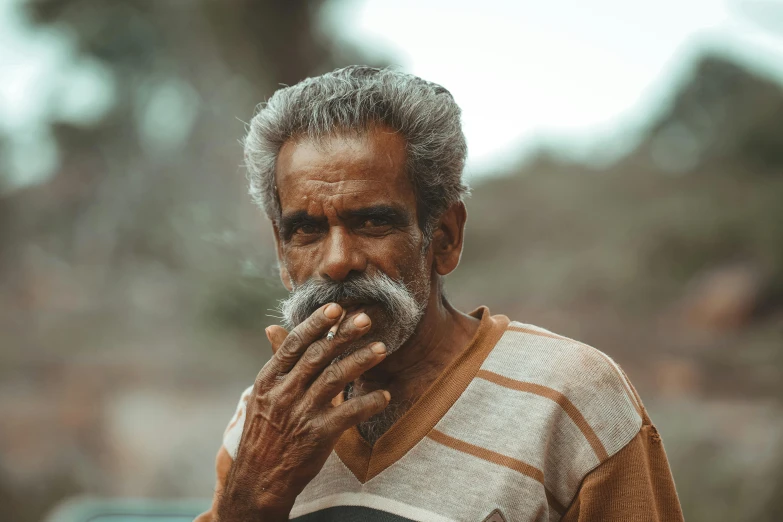 a man with grey hair and moustache holding his hand up to his mouth