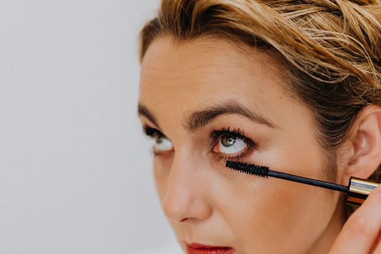 a young woman doing her eyeliner with the mascara on