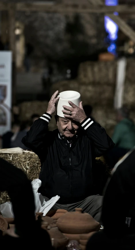 an old sailor covers his head while sitting in an auditorium