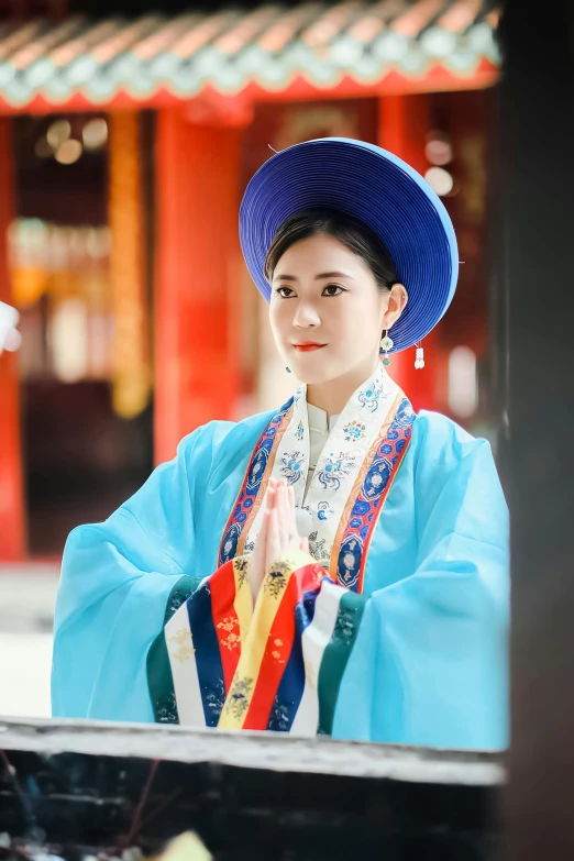 a women in an oriental outfit wearing a blue hat and holding soing in her hands