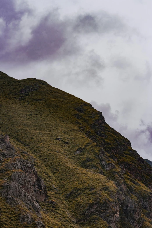 a hill covered in green grass with clouds in the sky