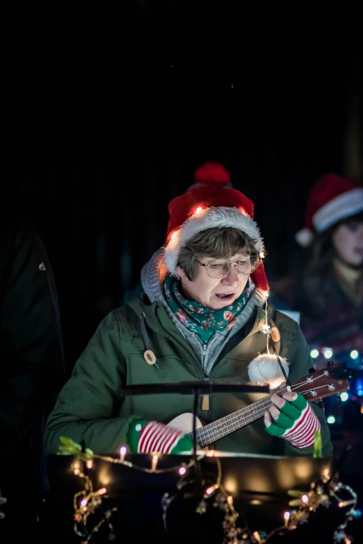 a person playing a guitar at night wearing a santa claus hat