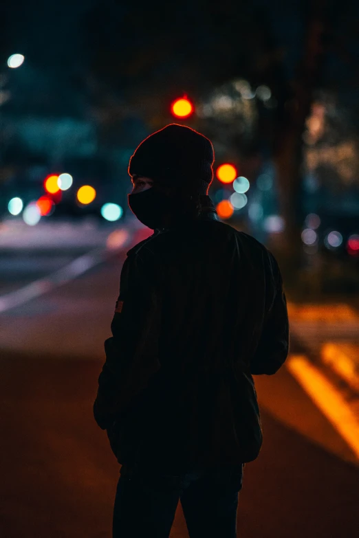 a person wearing a hat is standing on a street at night