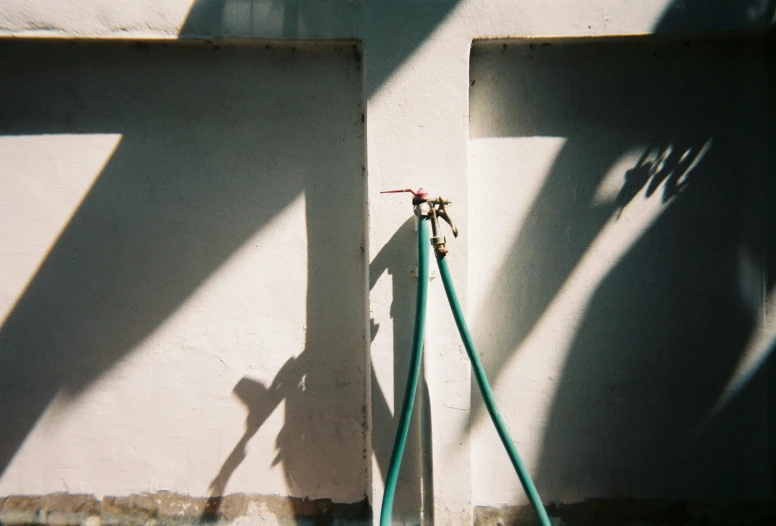 green pipes next to white wall on a cement ground