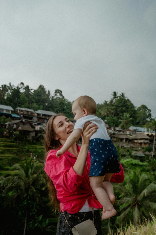 a young woman holding a small baby outside in a field