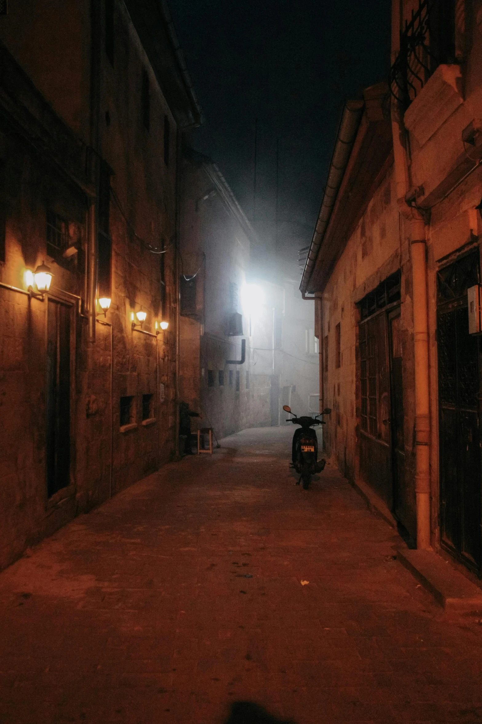 an alley with light bulbs shining down and a motorcycle parked next to it