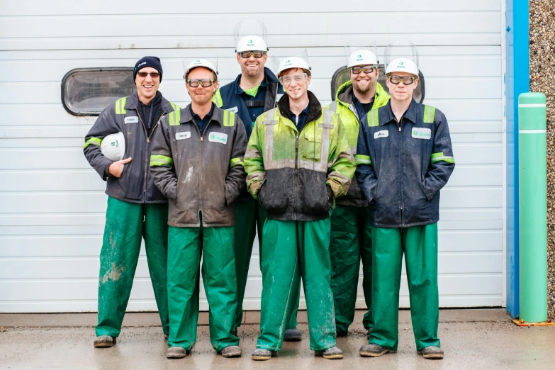 the workers are wearing green jackets and reflective helmets