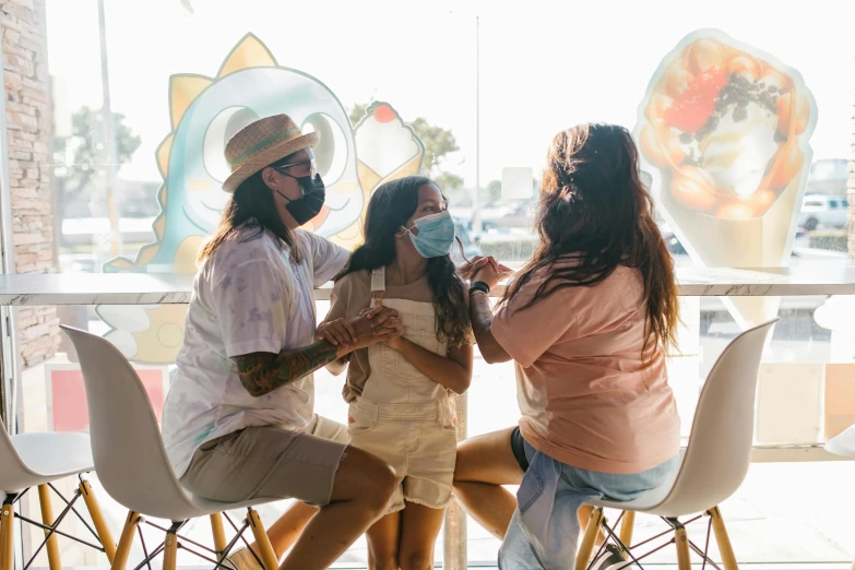 three woman sit at a table, while one woman holds soing in her hand