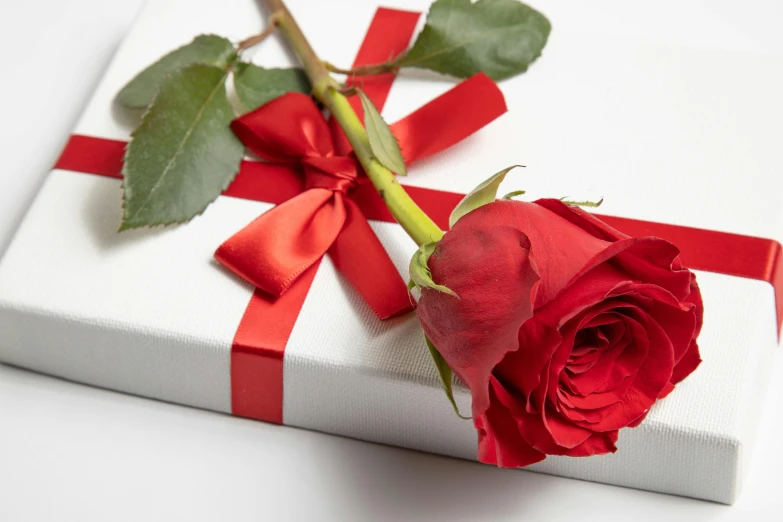 a single red rose sitting on a white box wrapped in red ribbon