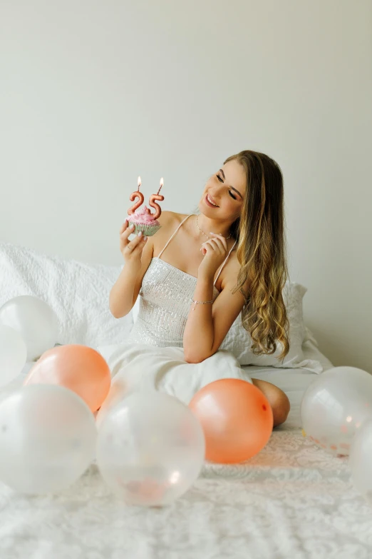a woman holding a cupcake over some balloons