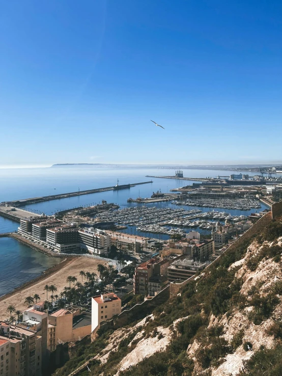 looking down at an area with lots of boats, buildings and a hill next to the ocean